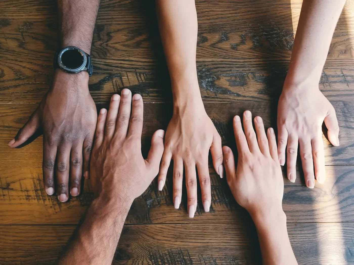 Several hands resting together on a wooden table.