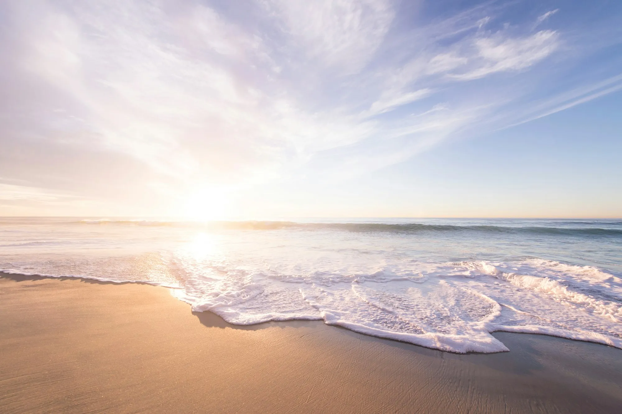 Gentle waves washing onto a quiet shoreline under a soft sunrise sky.