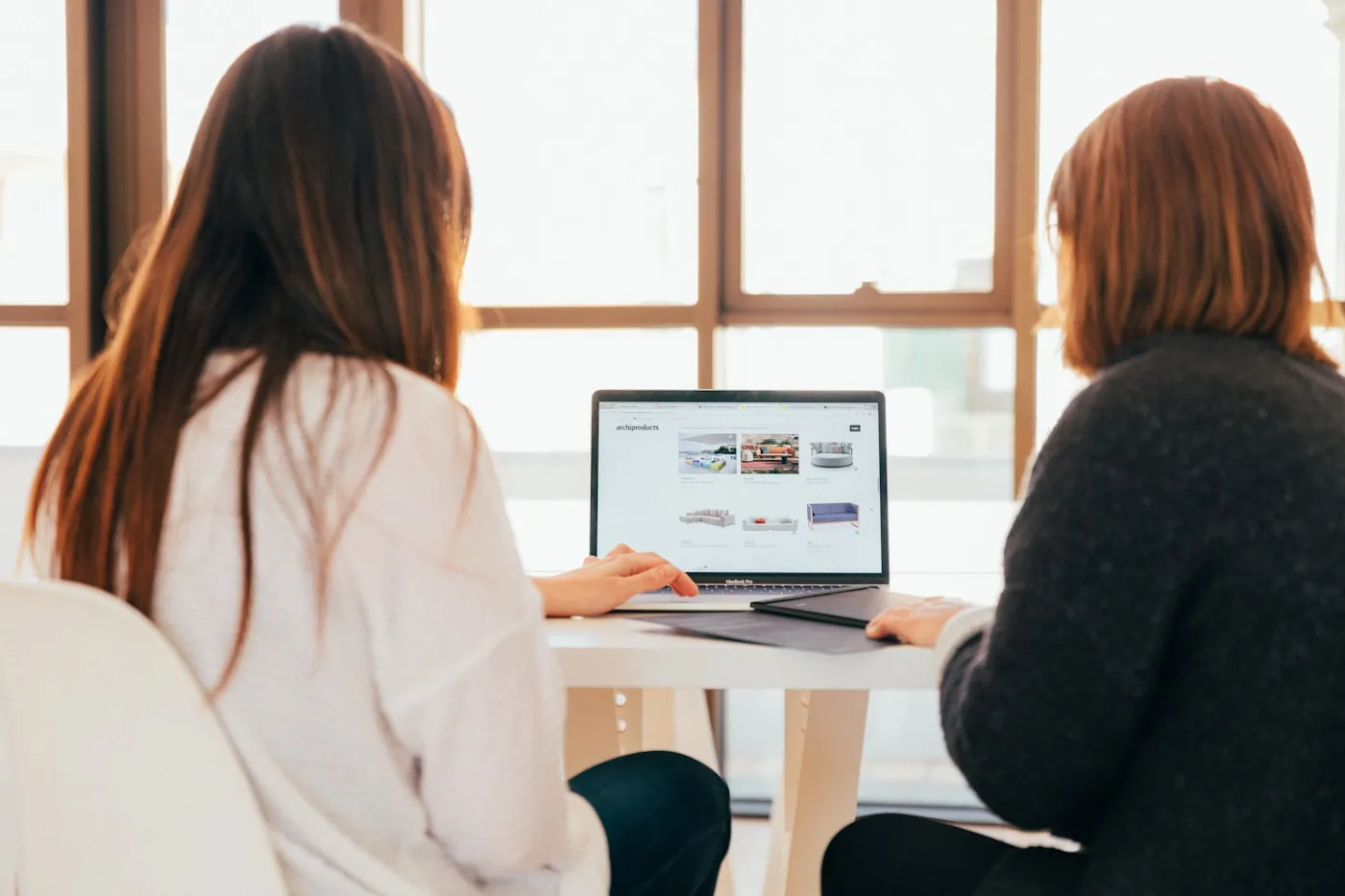 Two people working side by side at a sunlit desk.