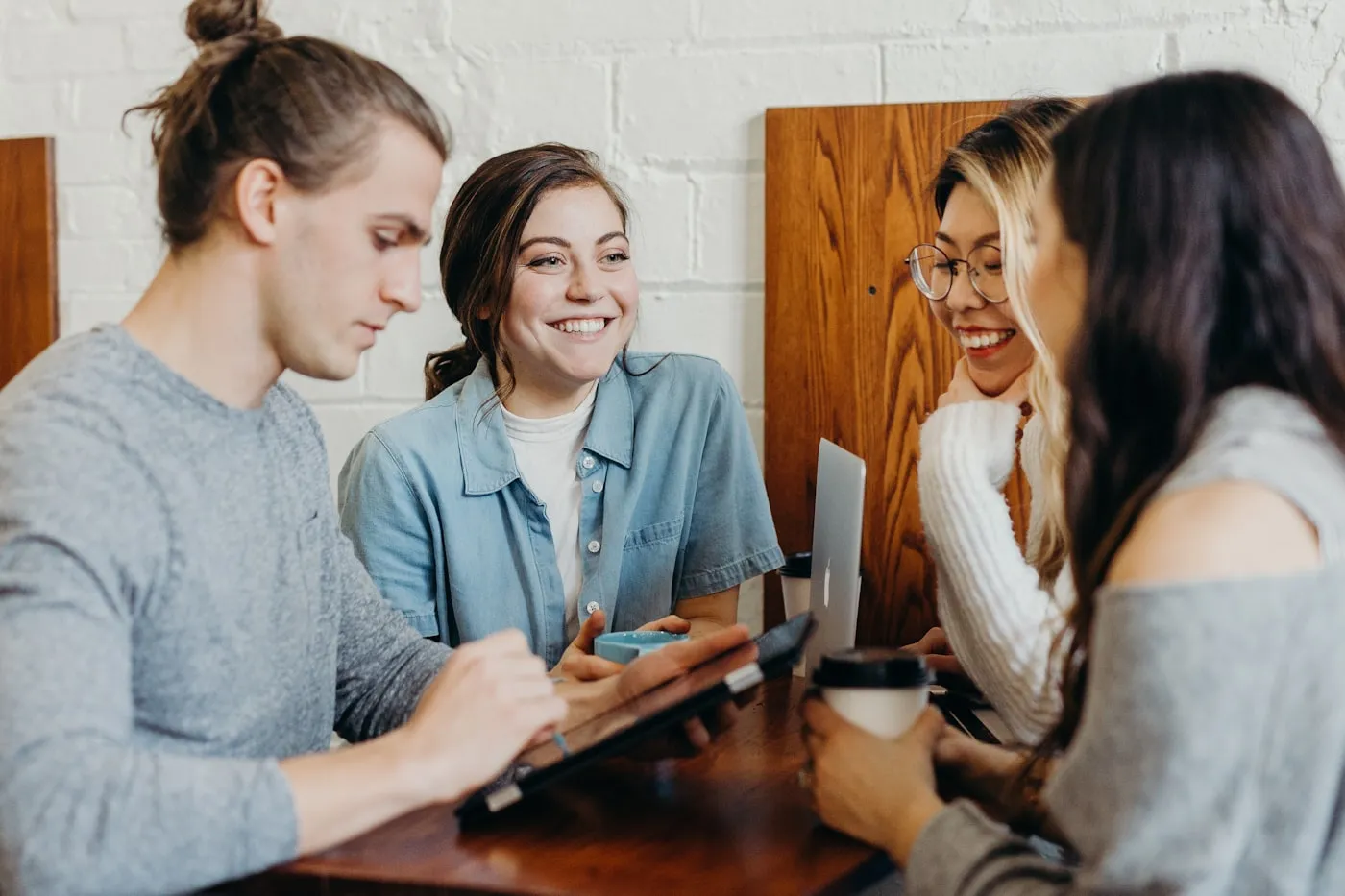 Three people talking together at a wooden table in a bright room.