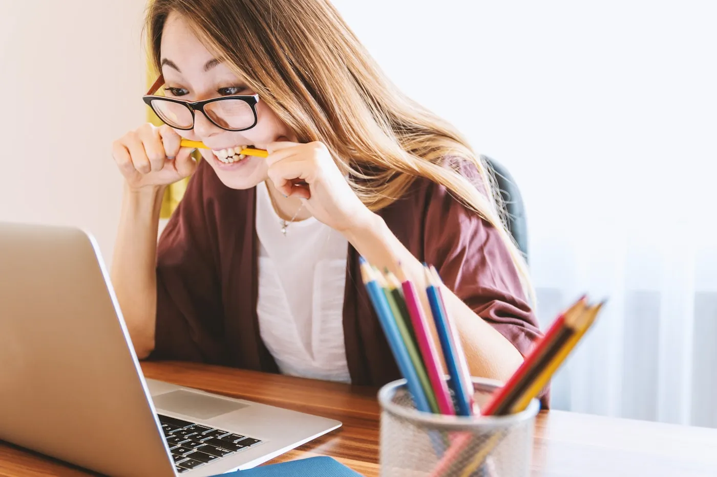A student smiling at a desk with a laptop and a cup of colored pencils.